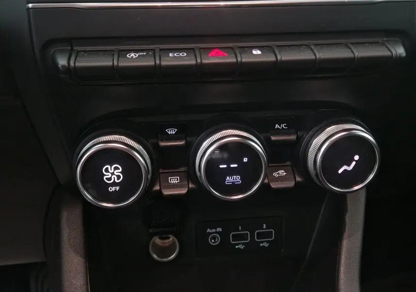 Gros plan sur la console centrale de la Renault Clio V gris platine, montrant les commandes de climatisation et les boutons de fonction.