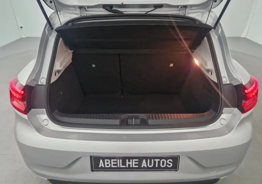 Coffre ouvert vu de l'arrière d'une Renault Clio V gris platine, montrant l'espace de chargement vide et l'éclairage intérieur.
