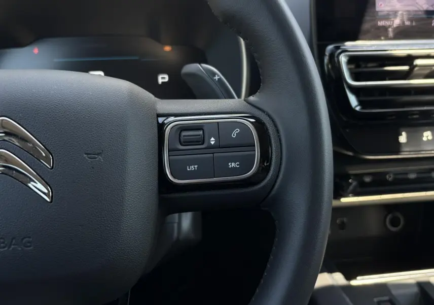 Gros plan sur le volant noir du Citroën C5 Aircross Hybrid 2025, avec commandes intégrées côté droit et tableau de bord partiel.