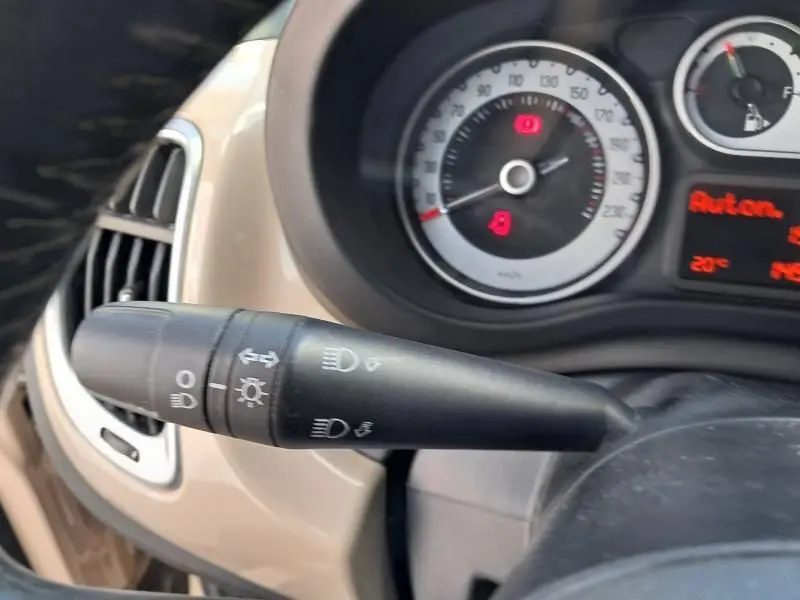 Gros plan sur la commande des phares et clignotants du tableau de bord beige d'une Fiat 500L 2014 diesel.