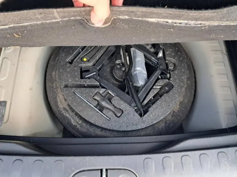 Vue du coffre de la Fiat 500L beige 2014, montrant la roue de secours et les outils de changement de pneu rangés sous le tapis.