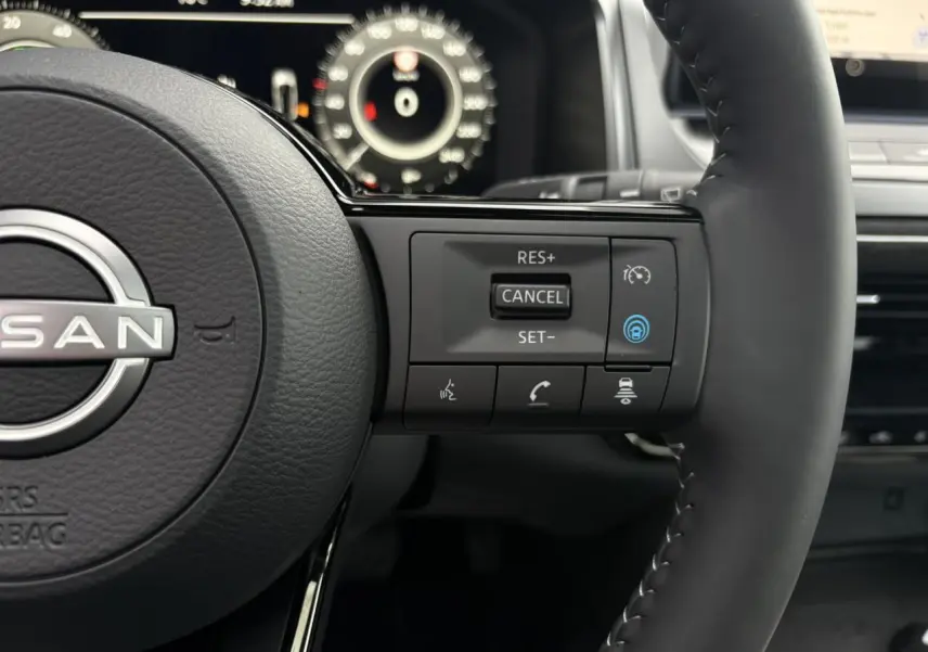 Gros plan sur le volant cuir noir du Nissan Qashqai 2025 avec commandes au volant et tableau de bord numérique en arrière-plan.