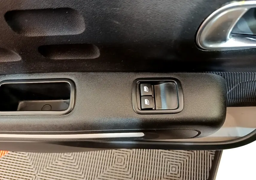Gros plan sur la commande des vitres électriques côté conducteur de la porte intérieure noire d'une Citroën C3.