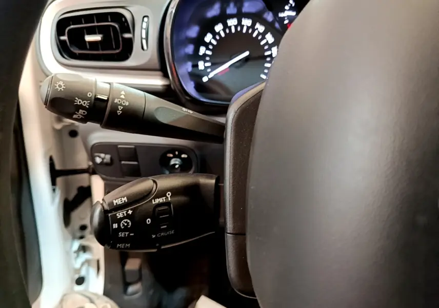 Gros plan sur les commandes au volant et le tableau de bord éclairé d’une Citroën C3 blanche, version Feel 2022.