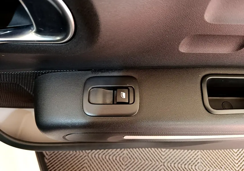 Gros plan sur la commande de lève-vitre noir sur la porte intérieure côté conducteur d'une Citroën C3 blanche.