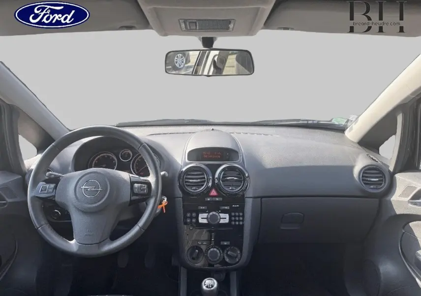 Vue intérieure avant de l’Opel Corsa noire de 2010, montrant le tableau de bord et le volant avec commandes intégrées.