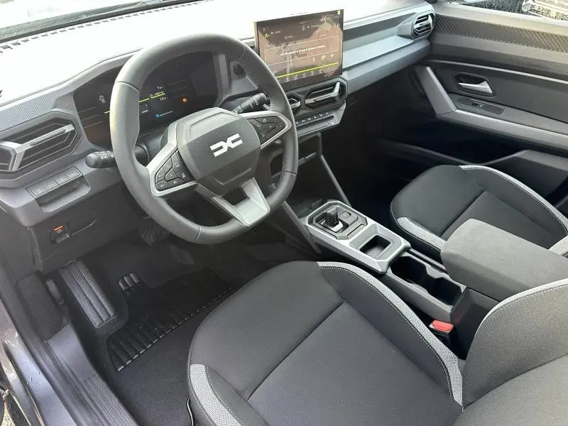 Vue intérieure côté conducteur du Dacia Duster 1.8 hybrid 2025, volant multifonction et écran tactile central visible.