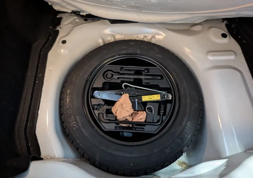 Roue de secours noire avec outils de changement dans le coffre blanc d'une Citroën C4 Cactus 2019.