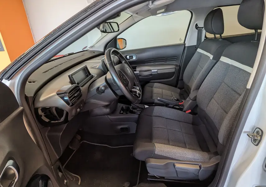 Intérieur côté conducteur de la Citroën C4 Cactus blanc 2019, sièges tissu gris avec bande claire et tableau de bord moderne.