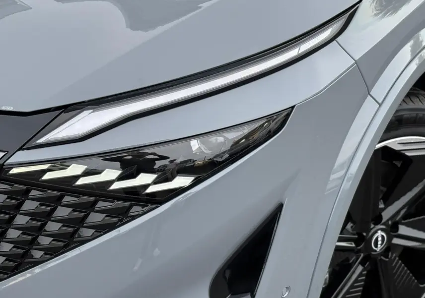 Gros plan sur le phare avant droit du Nissan Qashqai gris Ceramic avec calandre noire et jante alliage 20 pouces.