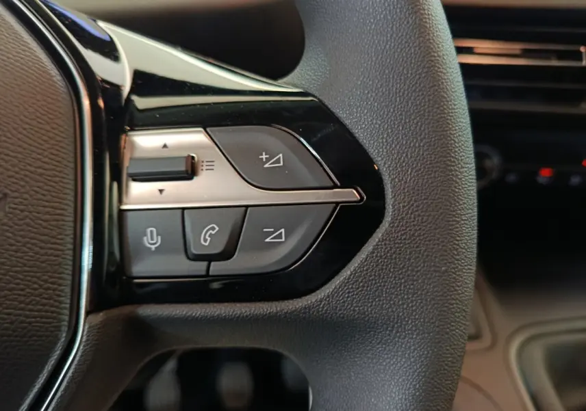 Gros plan sur les commandes du volant du Peugeot Partner blanc 2025, avec boutons de volume et téléphone.