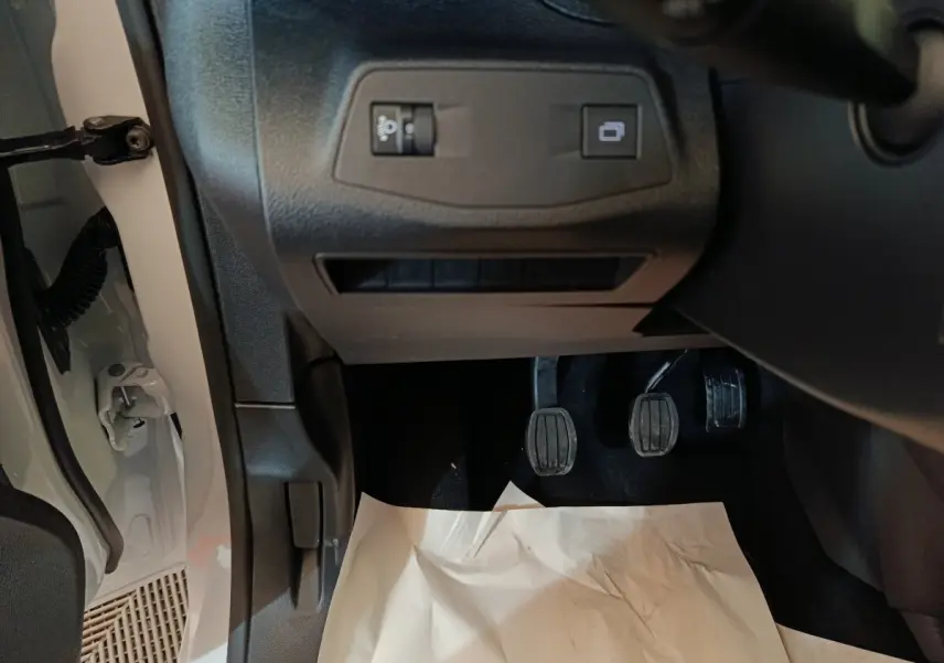 Vue intérieure côté conducteur du Peugeot Partner blanc 2025, avec pédales de boîte manuelle et commandes sous le tableau de bord.