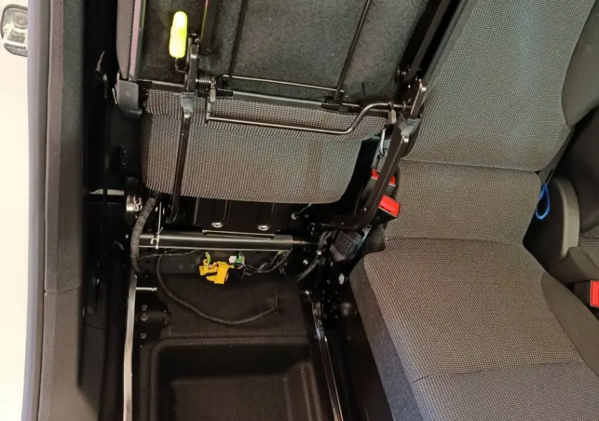 Vue intérieure rapprochée du siège passager relevé du Peugeot Partner blanc, montrant le rangement sous siège et la structure métallique.