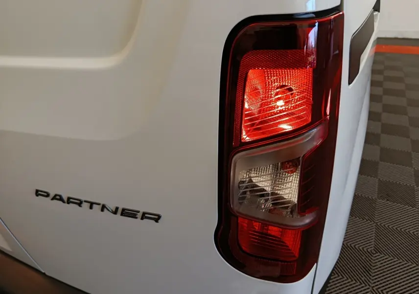 Gros plan sur le feu arrière droit et le logo PARTNER d’un utilitaire Peugeot Partner blanc, vue arrière droite.