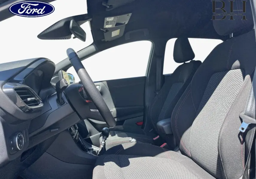 Vue intérieure côté conducteur du Ford Puma 2024, montrant les sièges en tissu noir avec surpiqûres rouges et la boîte manuelle.