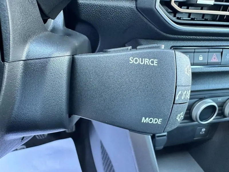 Gros plan sur la commande audio au volant de la Dacia Sandero beige Safari, avec boutons source et mode visibles.