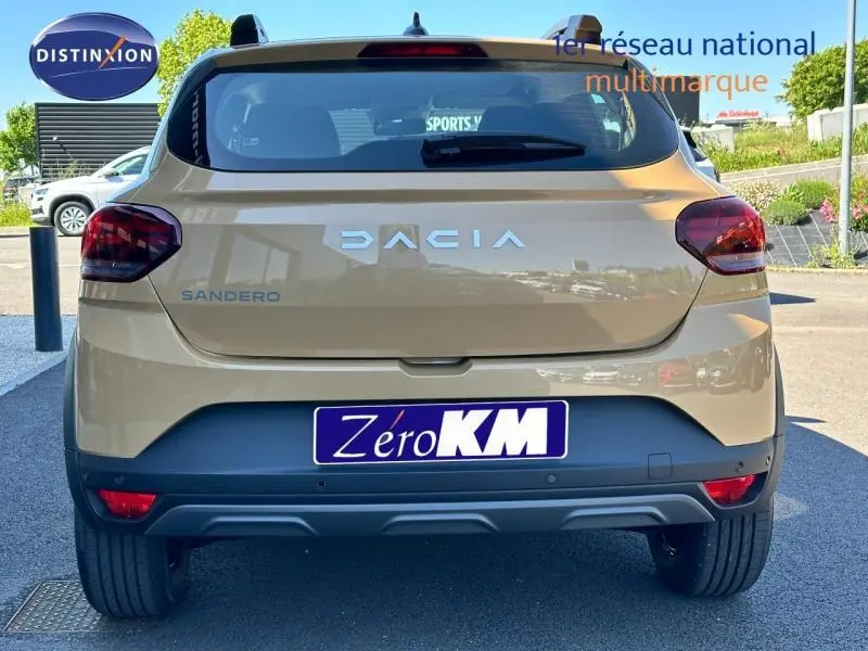 Vue arrière d'une Dacia Sandero beige Safari 2025 avec feux arrière foncés et barres de toit visibles.