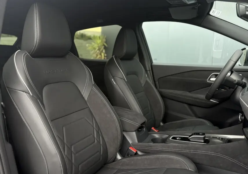 Intérieur du Nissan Qashqai 2025, vue côté conducteur, sièges Alcantara et cuir noirs avec surpiqûres blanches.