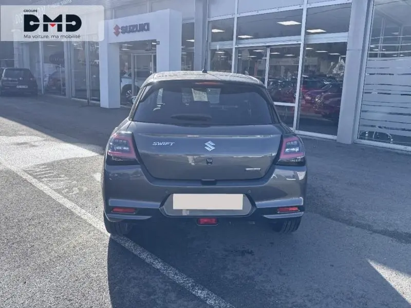 Vue arrière d'une Suzuki Swift 1.2 Hybrid 83ch Privilège 2024 en gris Mineral Gray Metal stationnée devant un showroom.