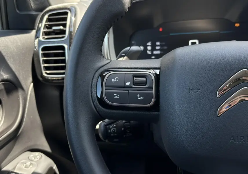 Gros plan sur le volant noir du Citroën C5 Aircross Hybrid 2025, avec commandes intégrées à gauche et aérateurs chromés.