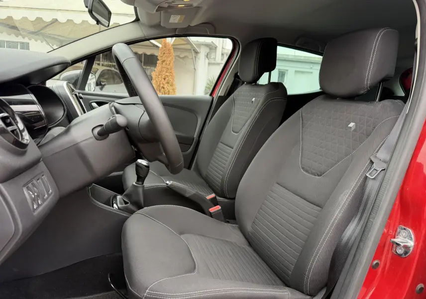Vue intérieure côté conducteur de la Renault Clio IV Limited TCe 90 rouge flamme, sièges tissu noir avec coutures blanches.