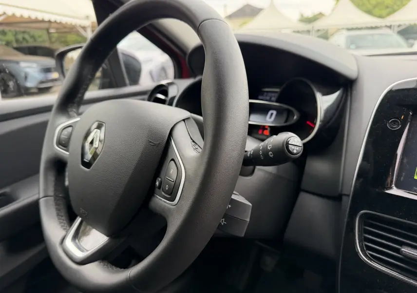 Gros plan sur le volant cuir noir de la Renault Clio IV Limited TCe 90, avec tableau de bord digital en arrière-plan.