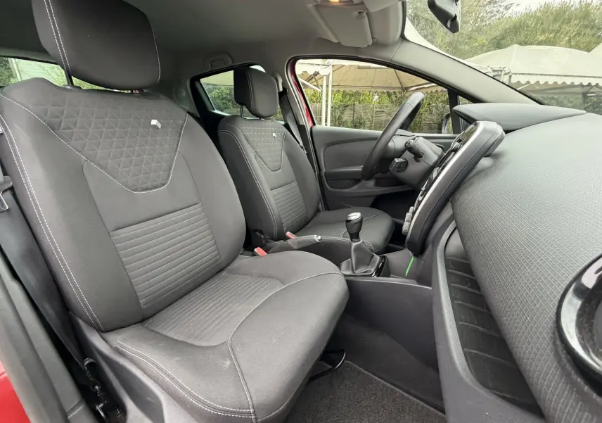 Vue intérieure côté conducteur de la Renault Clio IV Limited TCe 90 2017, sièges tissu noirs et volant cuir visible.