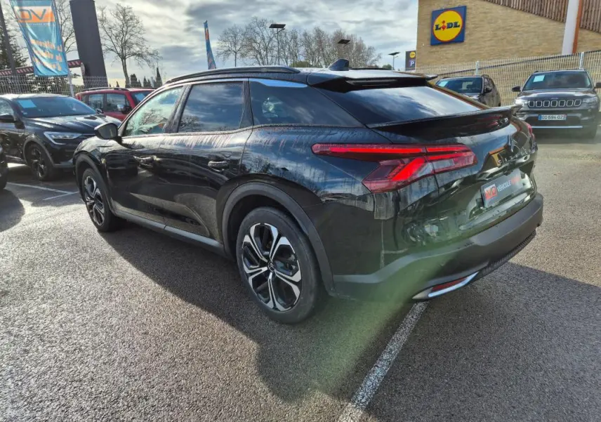 Vue 3/4 arrière droite d'une Citroën C5 X noire 2024 avec jantes alliage 19 pouces et antenne requin sur parking.