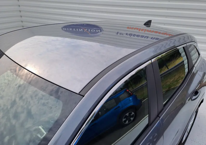 Toit et partie supérieure côté droit d'un Renault Austral gris schiste, avec reflet d'un autre véhicule bleu sur la vitre.