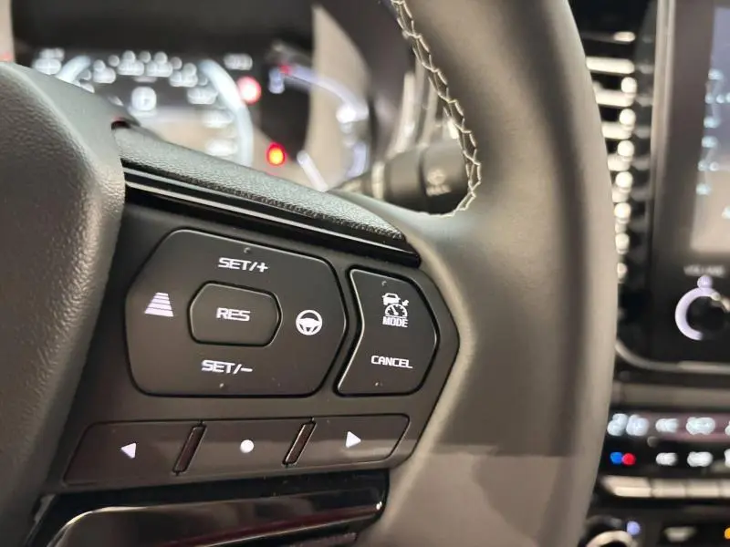 Gros plan sur les commandes au volant du pick-up Isuzu D-MAX 2025, finition Nitro Sport, avec cuir noir et éclairage blanc.