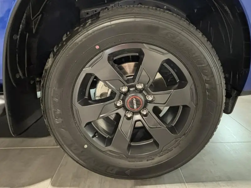 Gros plan sur la roue avant gauche d'un Isuzu D-MAX 2025 bleu Biarritz avec jante alu noire et logo central rouge.