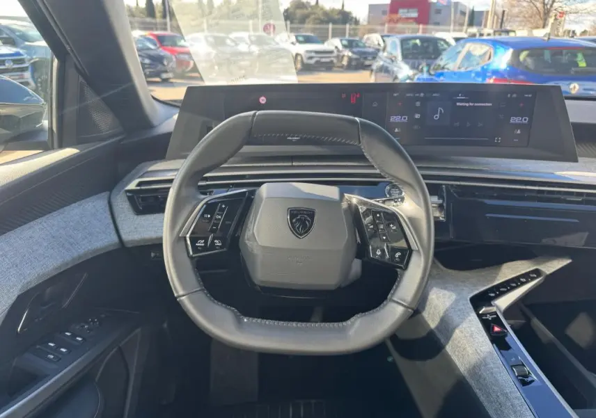 Vue intérieure centrée sur le volant cuir du Peugeot 5008 gris 2025 avec tableau de bord numérique et console moderne.