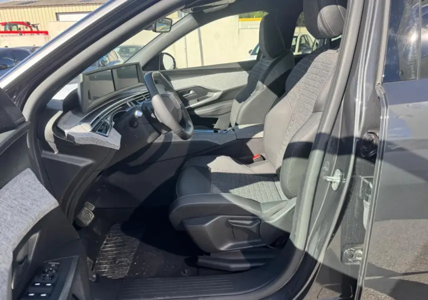 Vue intérieure côté conducteur du Peugeot 5008 Hybrid gris 2025, sièges tissu et cuir, tableau de bord numérique.