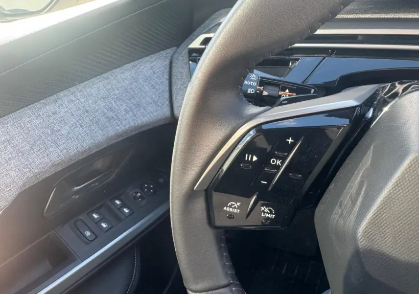 Gros plan sur le volant et la portière côté gauche du Peugeot 5008 gris, avec commandes au volant et boutons de vitres visibles.