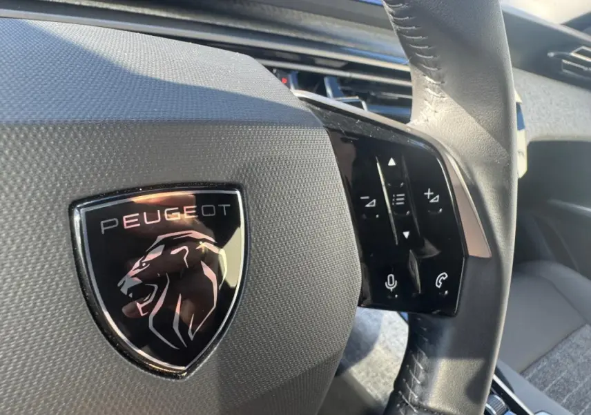 Gros plan sur le volant noir du Peugeot 5008 Hybrid 145 Allure avec logo lion et commandes tactiles à droite.