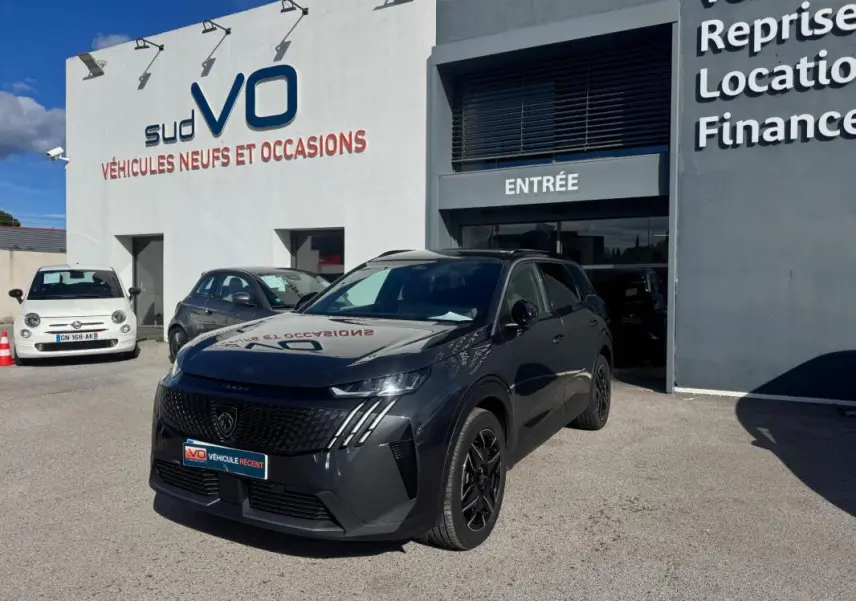 Peugeot 5008 Hybrid gris en 3/4 avant droit, avec jantes alliage noires de 19 pouces, devant un showroom.