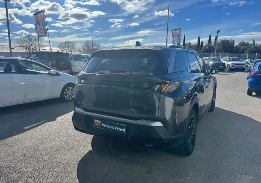 Vue 3/4 arrière droite d’un Peugeot 5008 gris 2025 avec feux arrière allumés et jantes alliage noires.