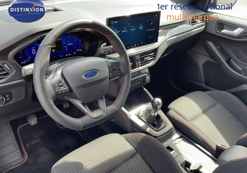 Vue intérieure de la Ford Focus SW 2023 montrant le volant, la console centrale avec boîte manuelle et les sièges tissu gris.