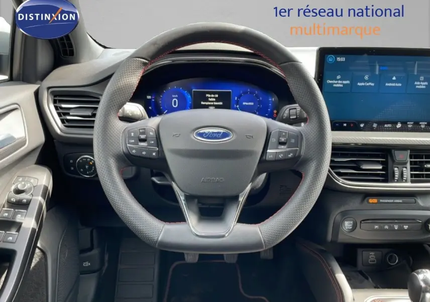 Vue intérieure avant centrée sur le volant cuir perforé avec coutures rouges, tableau de bord numérique et écran tactile Ford Focus SW gris lunaire.