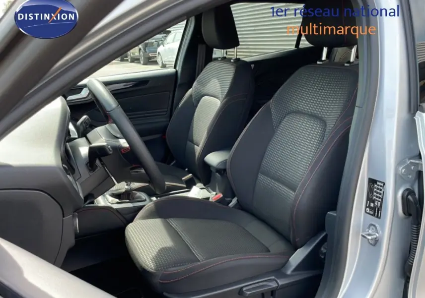 Vue intérieure côté conducteur de la Ford Focus SW gris lunaire, sièges tissu noir avec surpiqûres rouges visibles.