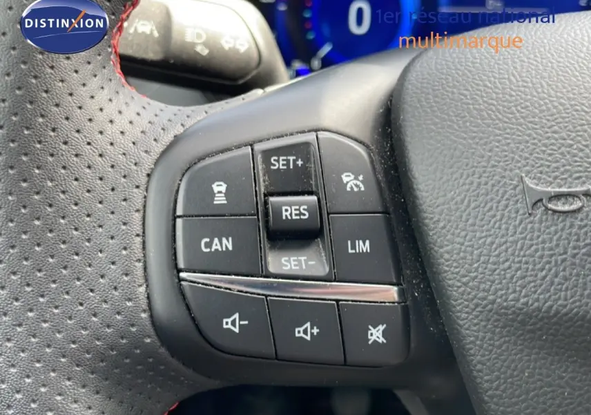 Gros plan sur les commandes noires du volant perforé avec surpiqûres rouges de la Ford Focus SW gris lunaire 2023.