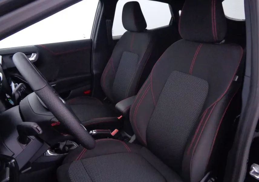 Vue intérieure côté gauche du Ford Puma 2022 noir agate, sièges tissu noir avec surpiqûres rouges et volant cuir perforé.