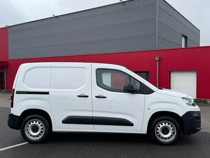 Profil droit d’un Citroën Berlingo Fourgon blanc Banquise avec portes latérales et jantes acier, sur fond industriel rouge et gris.
