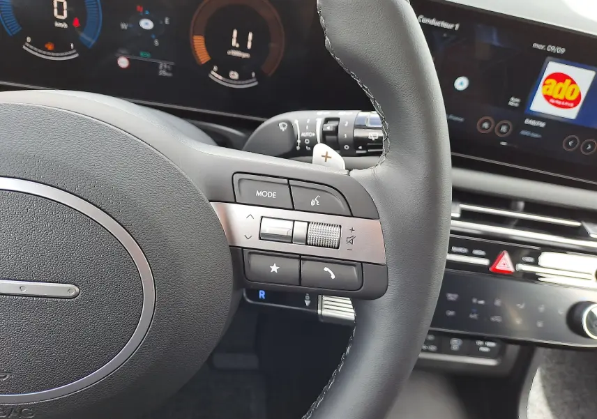 Gros plan sur le volant noir du Hyundai Tucson 2025 avec commandes intégrées et tableau de bord numérique en arrière-plan.