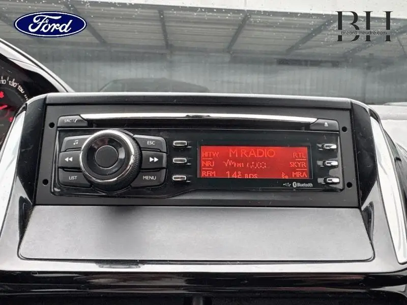 Tableau de bord avec autoradio numérique affichant plusieurs stations, intérieur d'une Peugeot 208 blanc banquise 2013.