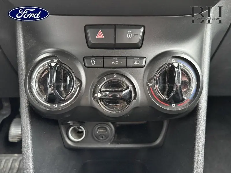 Tableau de bord central avec commandes de climatisation manuelle et boutons de sécurité d'une Peugeot 208 blanche de 2013.