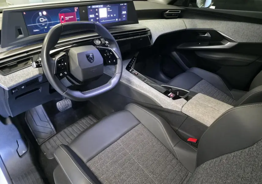 Intérieur avant droit du Peugeot 3008 blanc 2025, volant compact cuir noir, tableau de bord numérique et sellerie tissu gris.