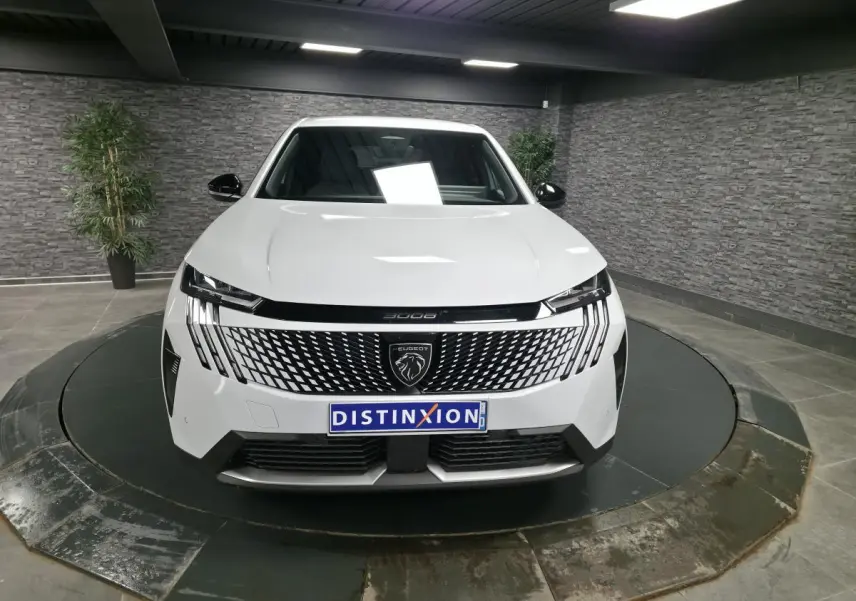 Peugeot 3008 blanc vue de face en intérieur avec calandre noire à motif géométrique et logo lion central.