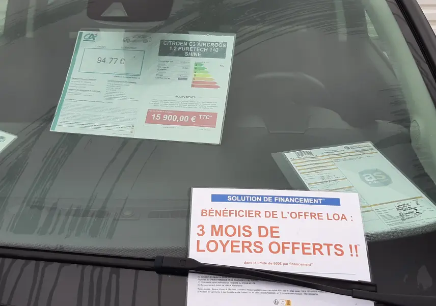 Vue avant rapprochée d'une Citroën C3 Aircross sable métal avec affiches de prix et promotion sur le pare-brise.