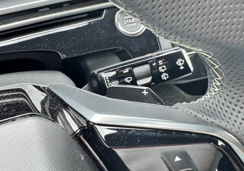 Détail du volant perforé avec surpiqûres et commandes, bouton start/stop et manette d'essuie-glace du Peugeot 5008 gris titane.